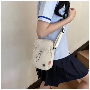 Detail van een minimalistische crèmekleurige nylon schoudertas gedragen door een studente.