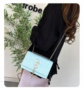 Detailweergave van een lichtblauwe gewatteerde crossbodytas met goud logo en kettingriem.