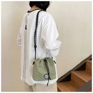 Dettaglio lifestyle di una borsa a secchiello in nylon verde con coulisse e logo sportivo