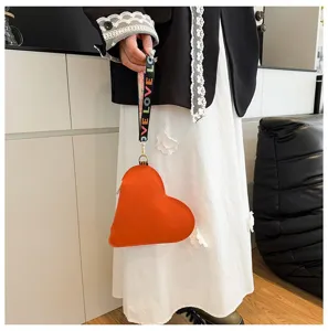 Primer plano de un bolso naranja en forma de corazón con correa estampada LOVE.