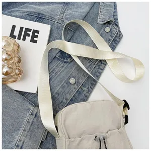 Detailopname van een minimalistische beige nylon crossbodytas met trekkoord op denim