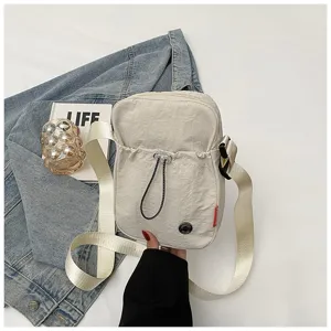 Detailopname van een crème nylon crossbody tasje gehouden tegen een denim achtergrond