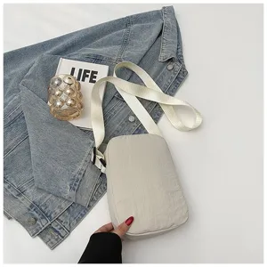 Detailweergave van het minimalistische beige nylon tasje tegen een denim achtergrond
