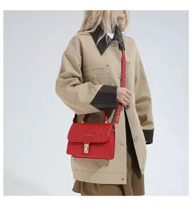 Modelo con un pequeño bolso de hombro cuadrado bordado rojo con cierre dorado.