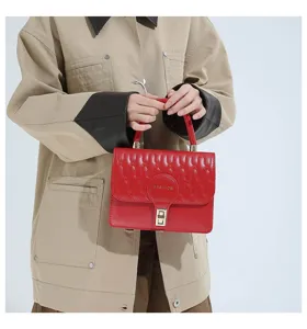 Detalle de un elegante bolso bandolera rojo bordado con un cierre dorado brillante.