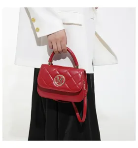 Detailansicht einer eleganten roten Stepptasche mit goldenem M-Logo in der Hand.