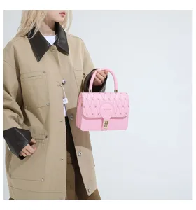 Detalle de bolso bandolera bordado rosa sostenido por modelo con chaqueta caqui.