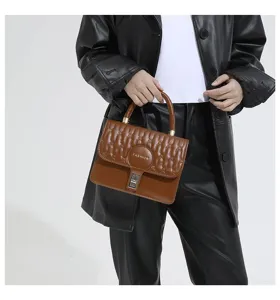 Detalle de un bolso bandolera acolchado marrón sostenido por una modelo con chaqueta