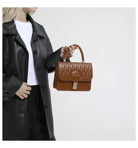 Detalle de bolso de mano bordado marrón con asa superior y elegante cierre