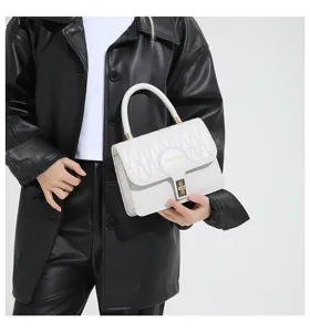 Detalle de un pequeño bolso de mano blanco bordado con cierre dorado y asa superior