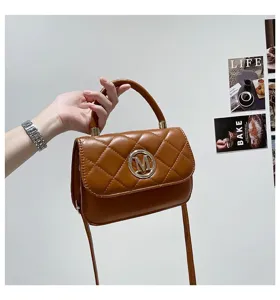 Detailansicht einer braun gesteppten Handtasche mit goldenem M-Logo aus Metall und Tragegriff.