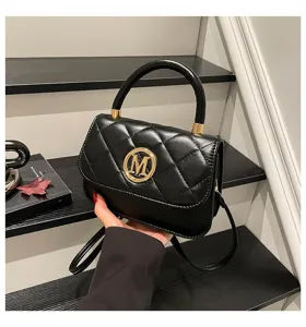 Detailansicht einer schwarzen gesteppten Umhängetasche mit goldenem M-Logo in der Hand
