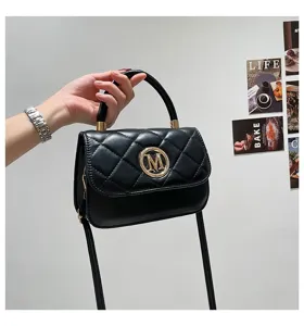 Handgehaltene Ansicht einer minimalistischen schwarzen Stepptasche mit goldener M-Schnalle.