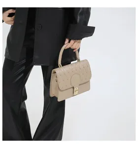 Detalle de un bolso bandolera pequeño cuadrado bordado beige sostenido por una modelo