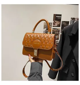 Elegante bolso de mano bordado marrón con cierre dorado y asa superior.