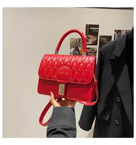 Detalle de un bolso bandolera bordado rojo con herrajes dorados y asa superior de