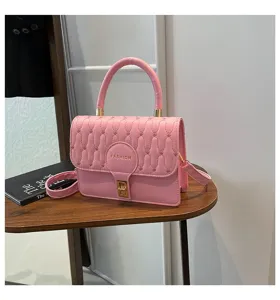 Vista detallada de un elegante bolso rosa bordado con herrajes dorados sobre una mesa.