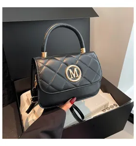 Nahaufnahme einer eleganten schwarzen Stepphandtasche mit goldenem M-Logo in Box