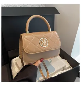 Nahaufnahme der beigen gesteppten Handtasche mit goldenem M-Logo auf Box-Hintergrund