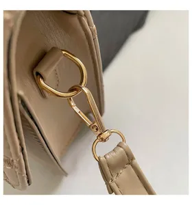 Detalle de los herrajes dorados y el bordado acolchado de un bolso beige