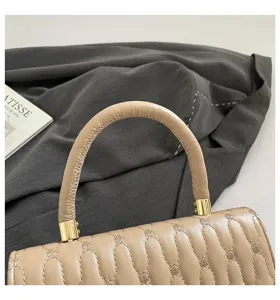 Detalle de la bolsa bordada beige que muestra el asa y los herrajes dorados.