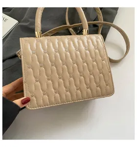 Primer plano de un bolso beige con bordado ondulado y elegantes herrajes dorados.