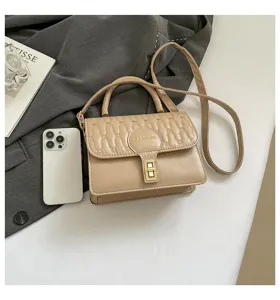 Detalle de un bolso pequeño bordado beige con asa superior y cierre dorado elegante.