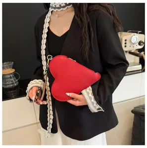 Primer plano de un elegante bolso de mano rojo con forma de corazón sostenido por modelo.