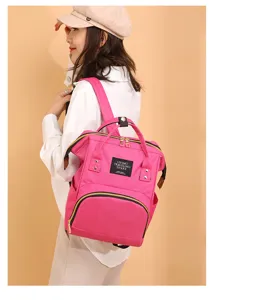 Vista detallada de una mochila maternal rosa llevada por una modelo sobre fondo beige.