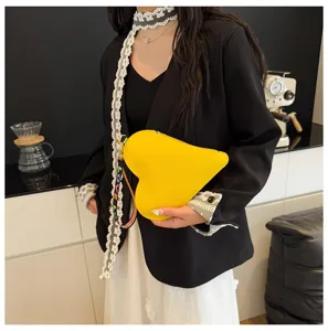 Vista detallada del bolso de mano amarillo con forma de corazón llevado por modelo.