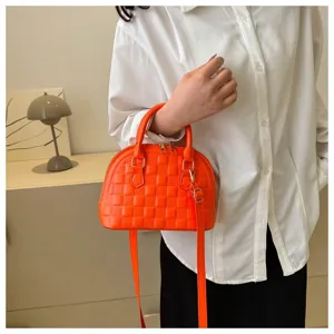 Un bolso de mano naranja vibrante con forma de concha sostenido por un modelo con camisa