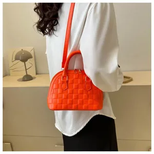 Detalle de un bolso de mano acolchado naranja brillante llevado al hombro por una modelo