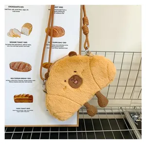 Detail view of a cute croissant-shaped plush crossbody bag with a capybara face design.