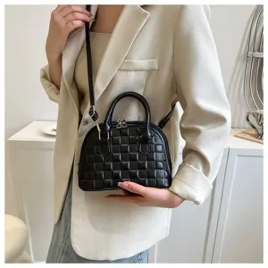 Detalle de bolso negro de mano tipo concha con textura de cuadros llevado por modelo.