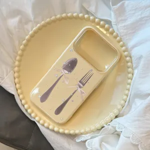 Gros plan de la coque iPhone crème avec illustration de couverts sur une assiette décorative.