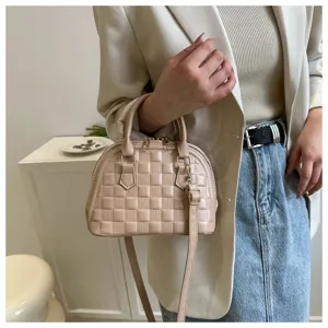 Vista detallada de un elegante bolso concha acolchado beige con herrajes dorados en mano.