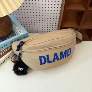 Close-up of a beige nylon chest bag with blue DLAMD print and fuzzy black charm.