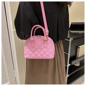 Detalle de un bolso de mano de concha rosa acolchado llevado al hombro por una modelo.