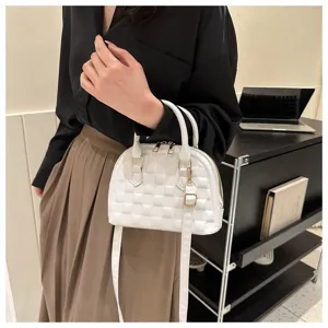 Elegante bolso de concha acolchado blanco sostenido por una modelo en un interior moderno.