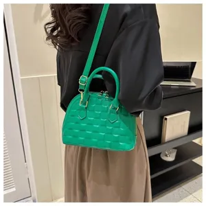 Vista detallada de un bolso tipo concha acolchado verde vibrante llevado por una modelo real.
