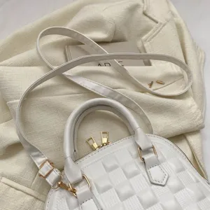 Detalle de un bolso de mano acolchado blanco con cremalleras doradas sobre tela
