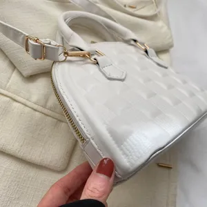 Primer plano detallado de un bolso concha acolchado blanco con cremallera dorada.