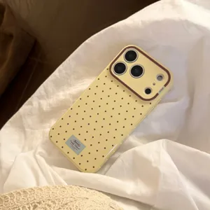 Gros plan d'une coque iPhone jaune crème à pois marrons sur des draps blancs doux