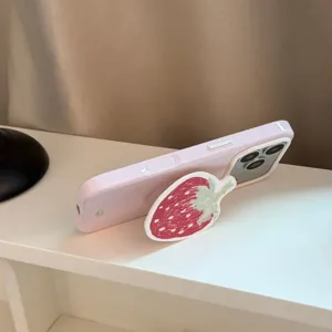 Détail d'un support de téléphone en forme de fraise rouge sur une coque iPhone violet lavande