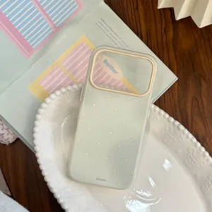 Vue détaillée d'une coque iPhone vert menthe à pois avec bord de caméra crème sur un plat