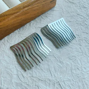 Detail shot of two minimalist silver wavy hair side combs on a white textured surface.