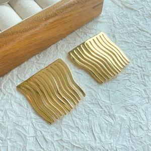 Detail shot of gold minimalist wave-patterned metal hair insertion combs on textured surface.