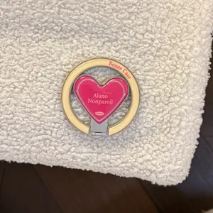 Close-up of pink heart-shaped phone ring holder on cream sherpa fleece phone case