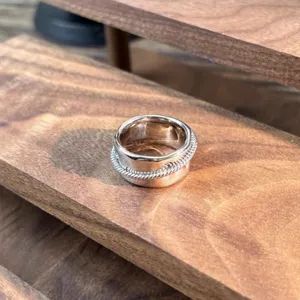 Detailaufnahme eines silbernen breiten Rings mit elegantem strukturiertem Seildesign