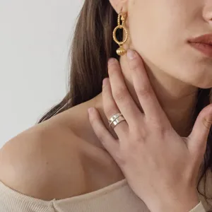 Makroaufnahme eines minimalistischen breiten Silberrings und goldener Creolen.